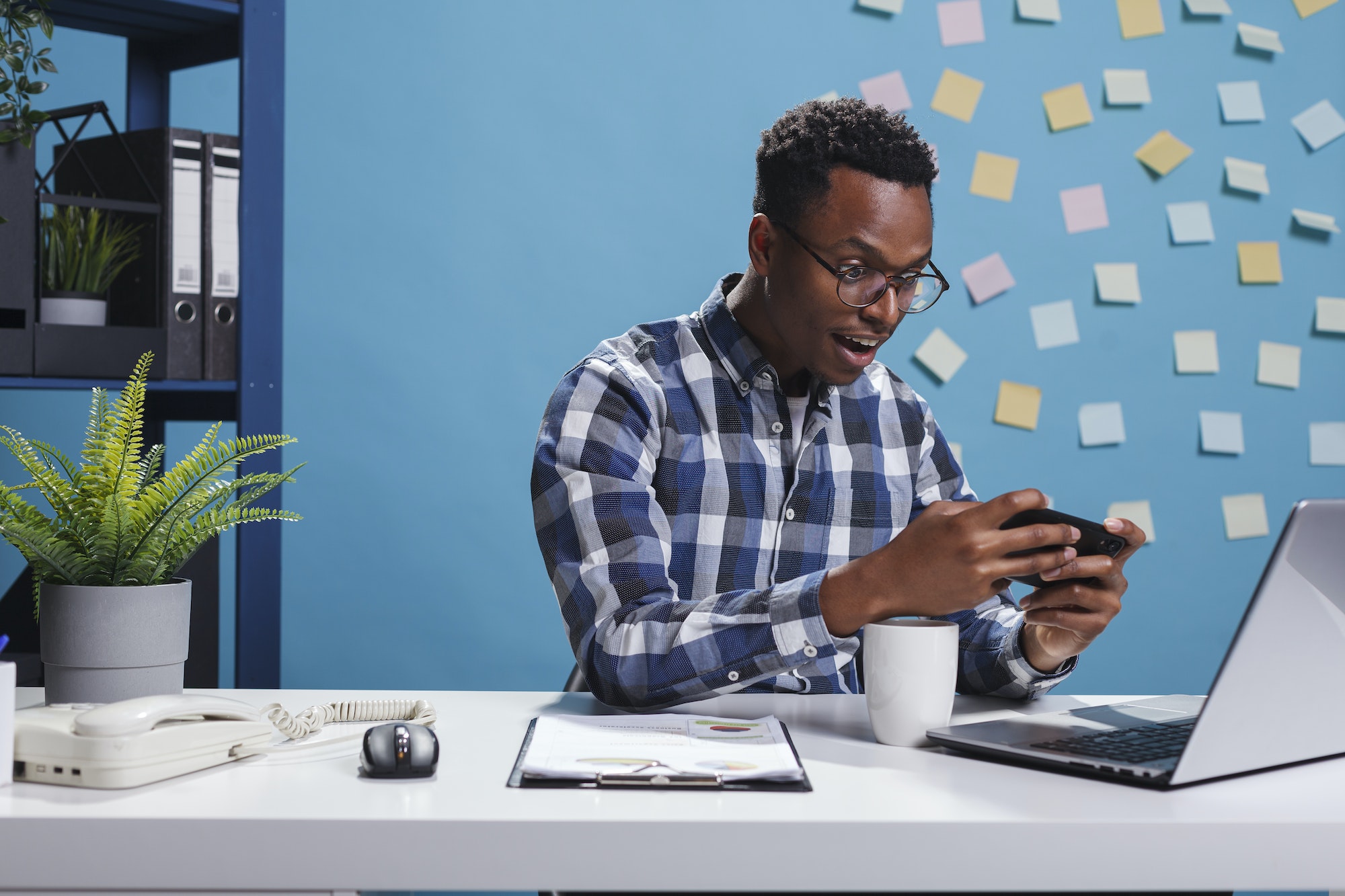 Happy cheerful business man playing games on smartphone device while in office workspace.