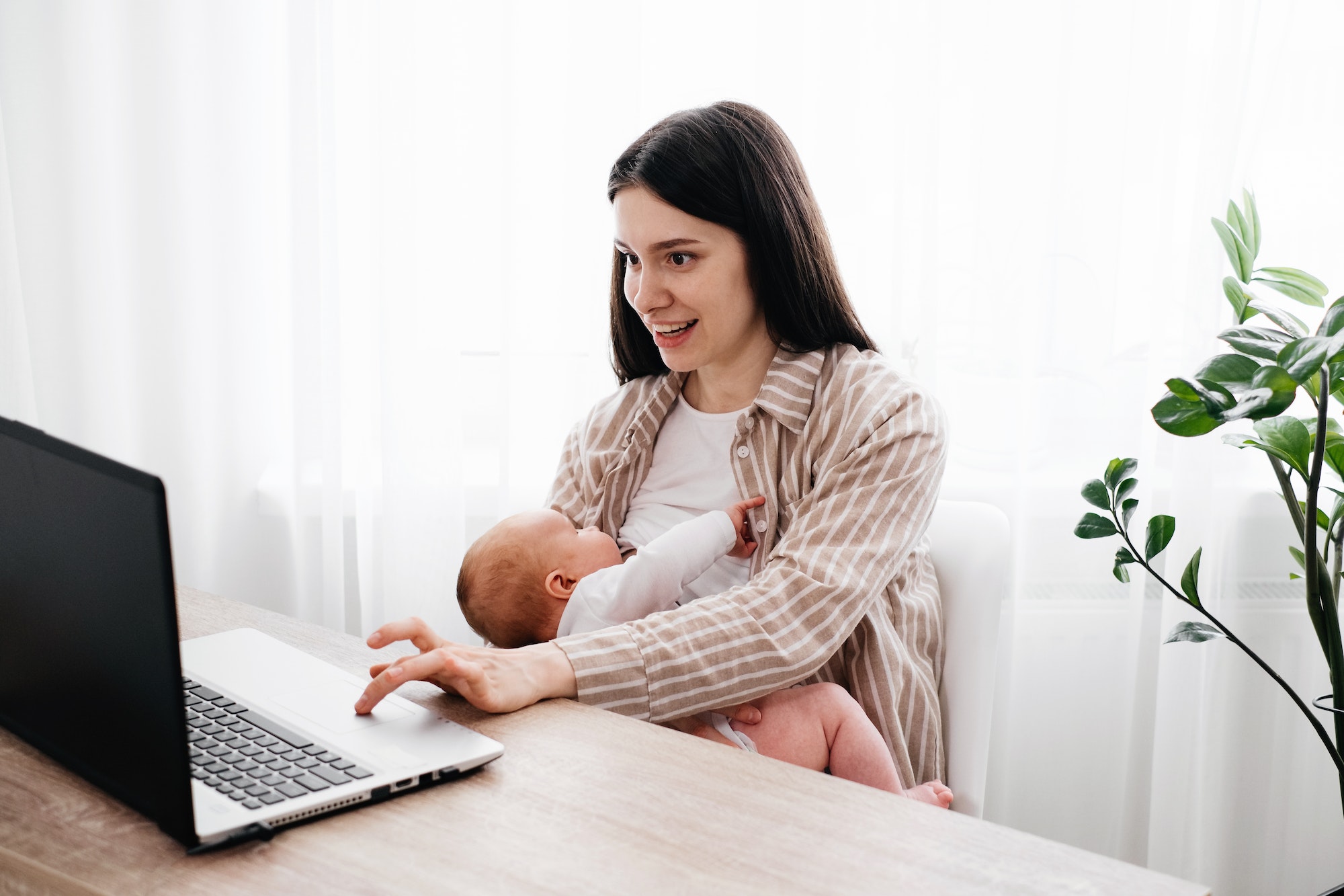 Working. breastfeeding woman with infant near laptop.